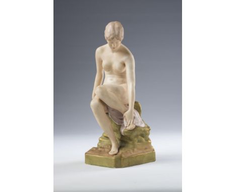 AN ART DECO ROYAL DUX BISQUE PORCELAIN FIGURE, modelled as a young female nude bather seated on a rocky outcrop, on a canted 