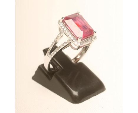 A RUBY AND DIAMOND RING, the emerald cut ruby of approximately 4.65cts claw set to a border of millegrain set small diamonds 