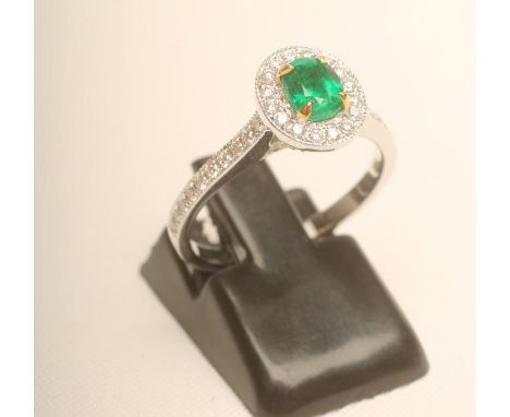 AN EMERALD AND DIAMOND CLUSTER RING, the oval facet cut Columbian emerald claw set to a border of numerous small millegrain s