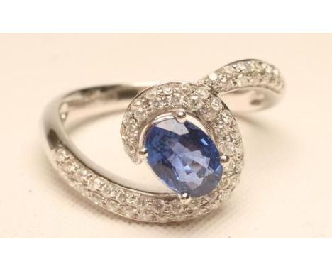 A SAPPHIRE AND DIAMOND DRESS RING, the oval facet cut sapphire claw set in a modern cross over millegrain set with numerous s