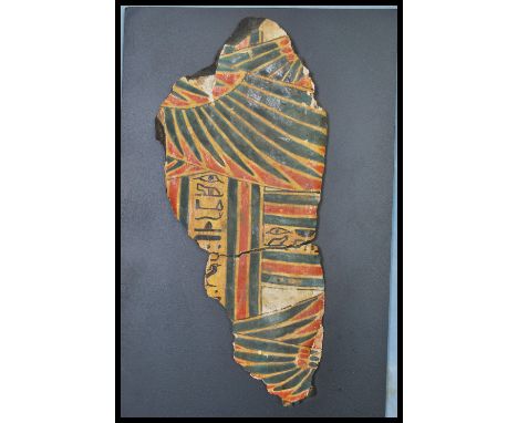 An Egyptian sarcophagus fragment being painted in red, blue and black with hieroglyphics and painted falcon wings with stripe