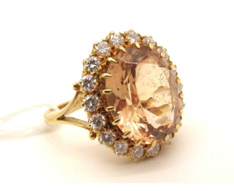 An 18ct Gold Peach Topaz and Diamond Cluster Dress Ring, (1977) oval claw set to the centre (stone scratched) within brillian
