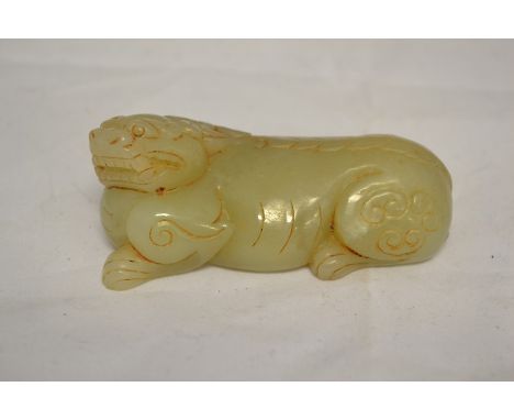 A Chinese archaistic jade carving of a crouching mythical lion with archaic 'C' scrolls on its hinds quarters, head turned to