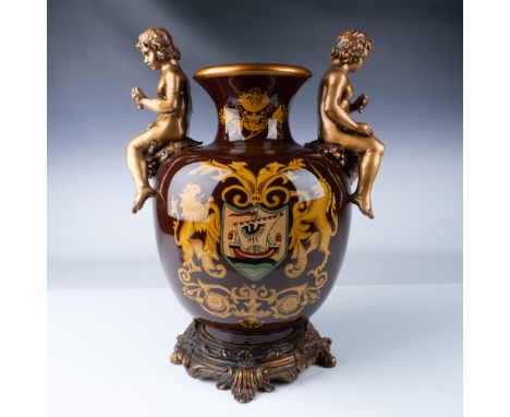 Elaborate decorative porcelain vase adorned with two golden cherub figures perched on either side, crafted with intricate gil