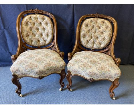 A pair of late Victorian carved walnut framed chairs with oval button backs and serpentine front seats upholstered in a flora