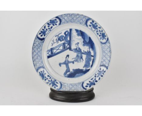 A Chinese Kangxi blue and white plate decorated with ladies at leisure, within a border of floral cartouches, on a diaper gro