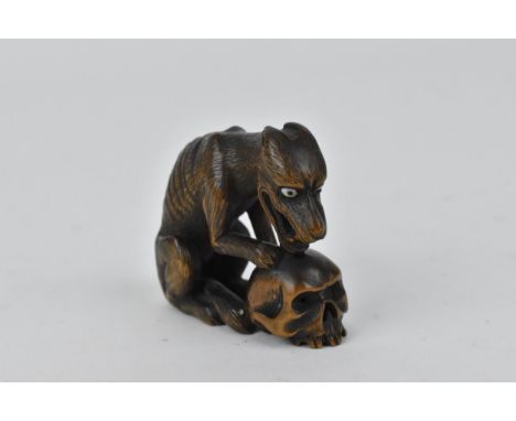 A Japanese carved wood netsuke, 19th century, modelled as a wolf and skull, with textured hair and inlaid eyes, unsigned, 4 c