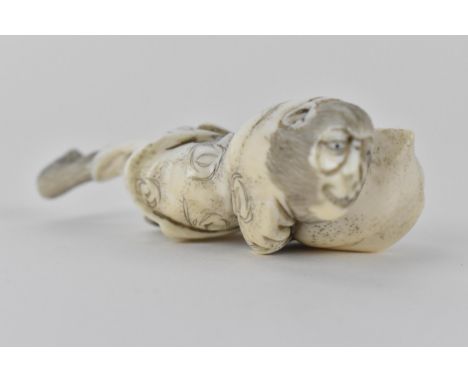 A Japanese Meiji period early 20th century ivory netsuke of a monkey wearing a nappy and clutching a large seashell, signed t