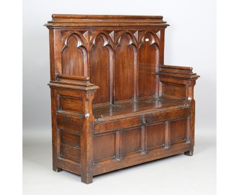 An early 20th century Gothic Revival oak settle, the heavily carved tracery panel back above a hinged box seat and ironwork h