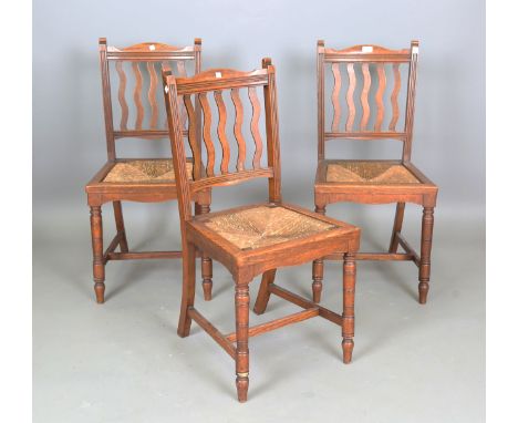 A set of three Edwardian Arts and Crafts oak-framed side chairs with wavy comb backs and inset rush seats, height 91cm, width