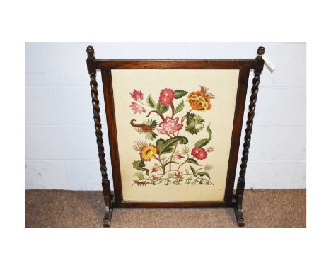 An early 20th Century oak firescreen, fitted floral needlework panel, barley-twist uprights on sledge feet, 74 x 94cms high.