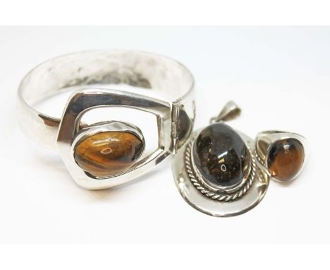 Three pieces of white metal jewellery set with quartz tiger's eye cabochons, comprising a bangle and a pendant both marked '9