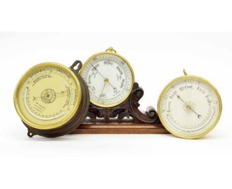 Circular barometer, within a brass casing and upon a carved wooden stand, 12" wide; also two other circular barometer/thermom