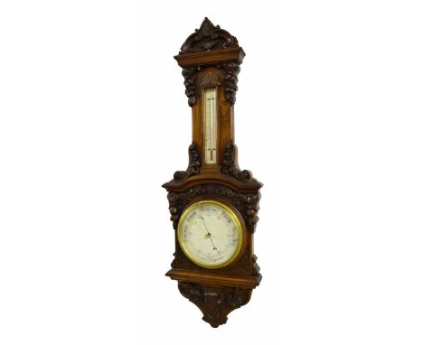 Walnut carved aneroid barometer/thermometer, the 8" silvered dial within an architectural foliate carved case under a thermom