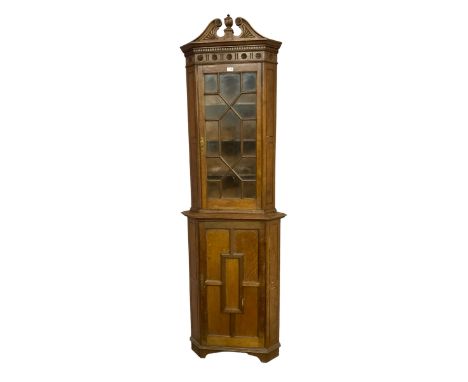 Early 20th century two-sectional oak corner cupboard, swan neck pediment with central architectural column finial, dentil cor