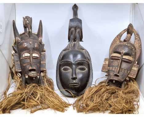Ethnographica:&nbsp;Three West African carved wood tribal masks,&nbsp;20th century, two with cowry shell, raffia and painted 