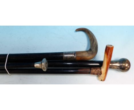 Two Edwardian ebonised walking sticks with white/yellow metal mounts; another with silver pommel; a swagger stick