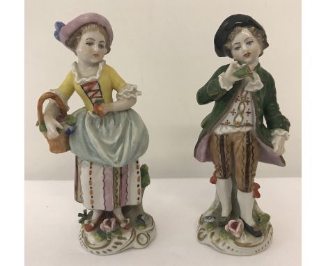 A pair of Sitzendorf German ceramic figurines of a boy and a girl carrying a flower basket.   Approx. 11cm tall.