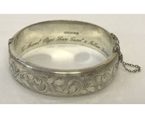 A vintage silver hinged bangle with half floral engraved decoration.  Complete with safety chain. Personal inscription to ins