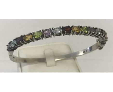 A white metal semi precious stone set bangle.  Half of bangle set with oval cut amethyst, blue topaz, citrine, peridot and ga