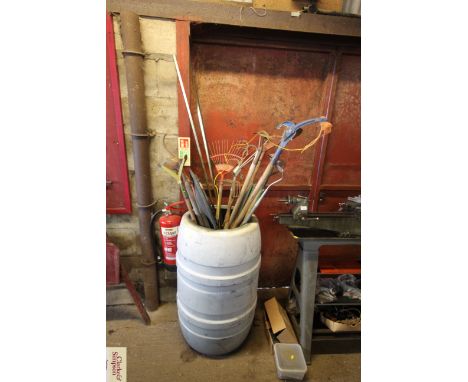 A water butt and contents of various long handled gardening tools