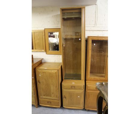 Modern Ercol light elm narrow side cabinet with a single glazed door enclosing wooden and glass shelves, the base with a sing