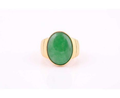 A yellow metal signet style ring set with an oval jade cabochon measuring 20mm x 15mm, the tapering reeded shank stamped 750,