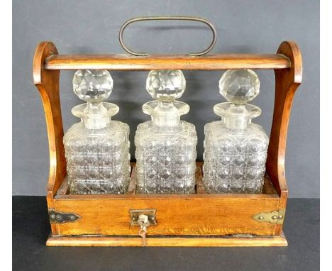 A Victorian oak three bottle tantalus, with plated mounts, containing three hobnail cut square glass decanters and stoppers, 