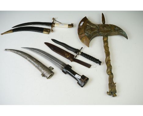 A collection of three sheathed daggers to include two arabic examples together with a brass axe. 