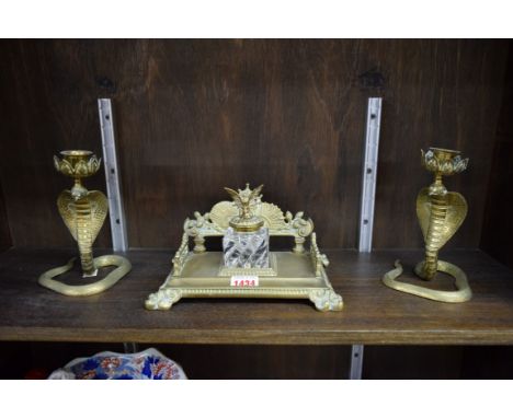 A Victorian cast brass inkwell, 21cm wide; together with a pair of brass serpent form candlesticks, each with inset red eyes,