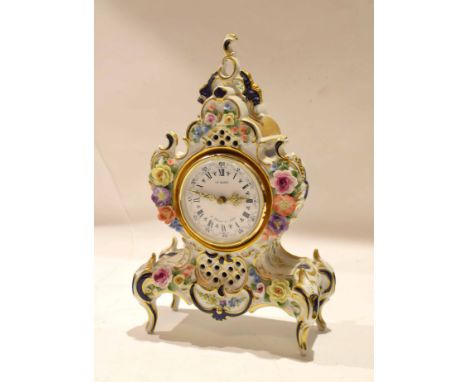 Porcelain clock case containing a clock, the dial picked out in Roman numerals with gilt hands, the case with applied floral 