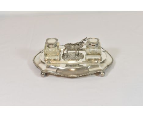 An antique/vintage silver plated double inkwell desk stand the shaped stand raised on four ball feet, surmounted with a stag 