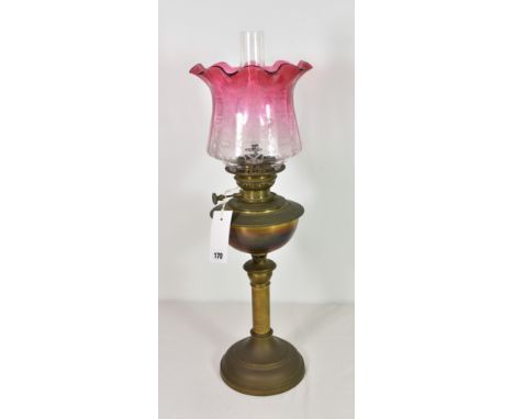 An antique brass oil lamp with etched cranberry glass shade