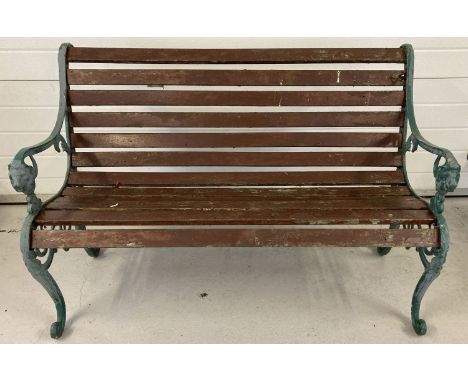 A wooden slatted garden bench with cast iron bench ends painted green and with lions head detail.  