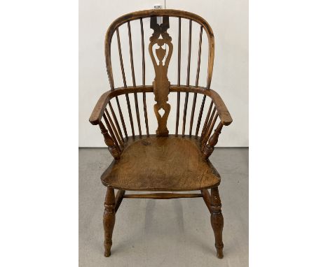 An antique elm seated spindle back Windsor armchair with carved back panel and turned legs.  