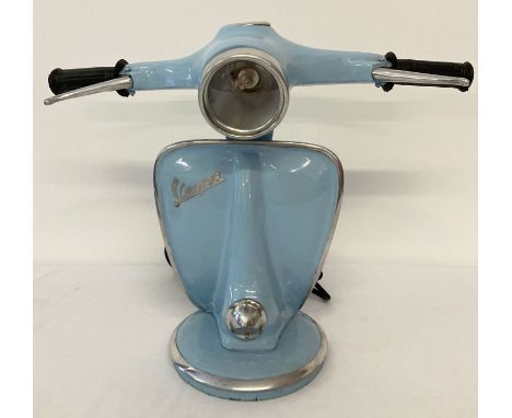 A novelty table lamp in the shape of the handlebars of a Vespa scooter, in pale blue.  With moving brake levers and speedomet