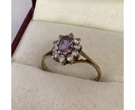 A 9ct gold dress ring set with central oval purple cubic zirconia.  Surrounded by 10 smaller round cut clear cubic zirconia s