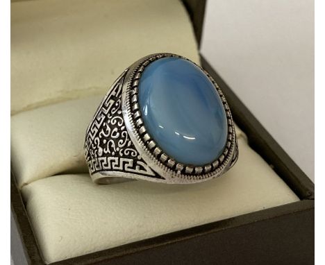 A men's silver dress ring set with a pale blue cabochon stone. Greek key detail to both shoulders.  Marked 925 to inside of b