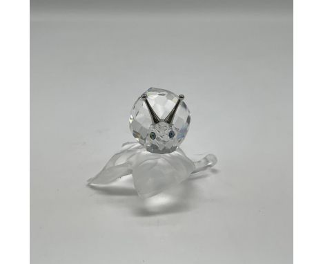 Depicts clear snail with crystal shell on top of opaque vine leaf. Rhodium antennas on top. Cantaloupe colored eyes with blac