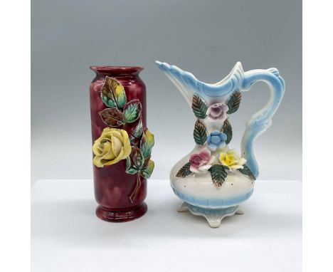 2 hand made and hand decorated vessels adorned with raised flowers. A burgundy vase with a yellow rose, and a white and blue 