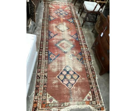 An Antique Caucasian brick red ground runner 336cm x 110cm, severely worn and holed