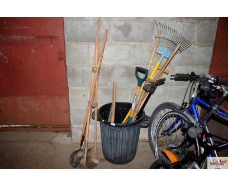 A plastic dustbin containing various long handled tools and a bunch of brushes etc