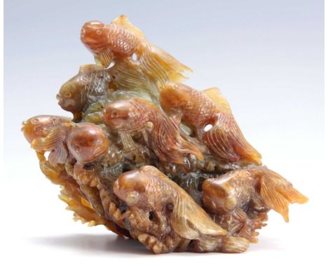 A LARGE JADE TYPE PALE GREEN AND AMBER GROUP OF SWIMMING FISH amidst lapping waves and seaweed, 26cm across 19cm high.