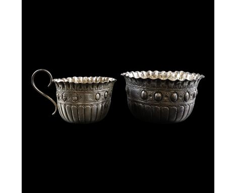 A late Victorian silver cream jug and sugar basin, each having a cusped everted rim and decorated with lobes and a band of ov