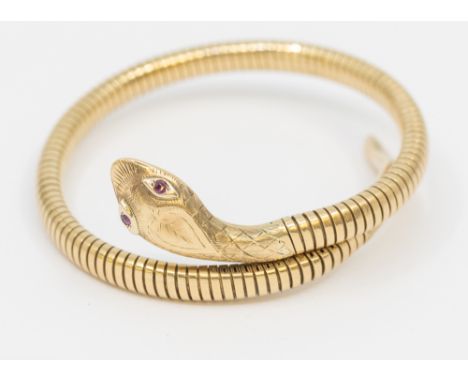 A 9ct gold serpent bangle, comprising a coiled form, the head with small ruby set eyes and engraved decoration, steel core, t