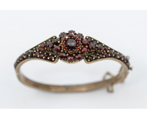 A Victorian Bohemian garnet metal hinged bangle, comprising a central flower motif set with rose cut garnets, width approx 16