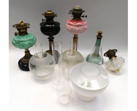 A collection of four late 19th/early 20th century oil lamps to include; a green glass and brass columned with shade and funne
