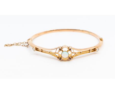 An Edwardian opal and ruby set 9ct rose gold hinged bangle, comprising an open work quatrefoil motif set to the centre with a
