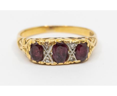 A ruby and diamond 18ct gold three stone ring, comprising three oval rubies, diamond accents to a scrolled mount, width appro