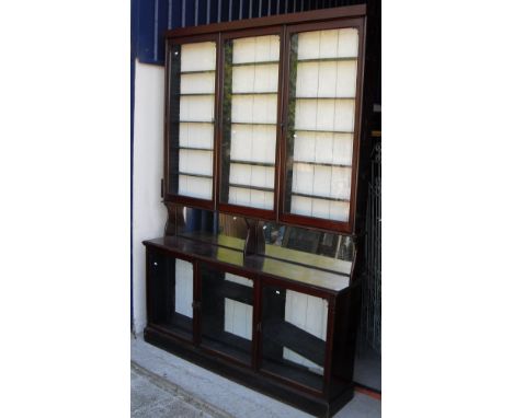 A Victorian mahogany apothecary cabinet with three large glazed doors enclosing adjustable shelving on a base with mirrored b